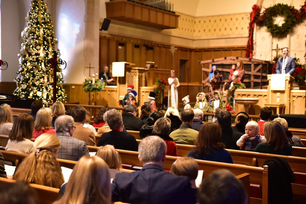 people in pews facing altar space decorated with christmas tree and nativity scene.